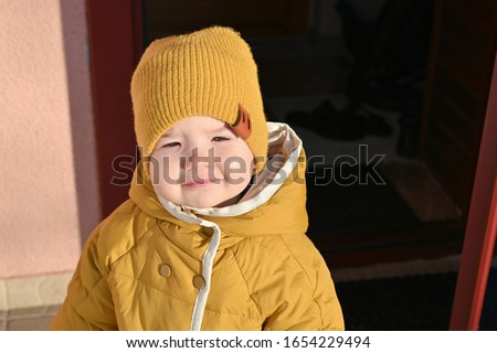 A child in yellow clothes. Dressed in a warm hat and jacket. The sun shines on a childs face.