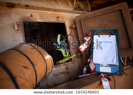  
Wide angle pic of permit to work paper clipping on isolation control permit board together with red personal danger locks and tags at confined space entry exit door ventilation fan                  