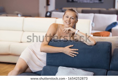 Cheerful woman buyer sitting on sofa with pillow in furniture shop