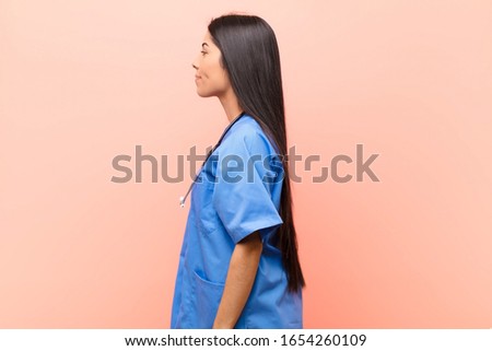 young latin nurse on profile view looking to copy space ahead, thinking, imagining or daydreaming against pink wall