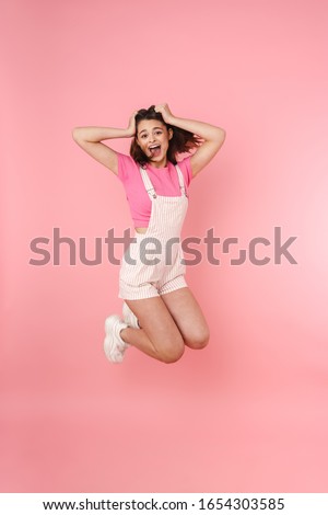 Full length of a pretty excited young teenage girl jumping isolated over pink background, rejoycing