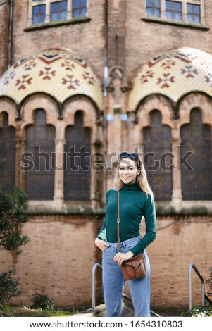 Young blonde woman standing near old building in Europe and wearing green turtleneck sweater. Concept of european architecture and traveling.