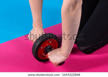 girl athlete holds a roller to strengthen the muscles of the abs and back, performs exercises, on a pink mat, sports concept