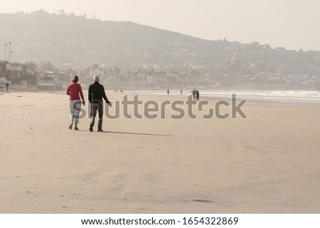 Couple walk on beach at sunrise, with misty city skyline behind and morning mist covering mountains, La Jolla, San Diego CA