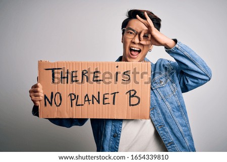 Young handsome chinese activist man protesting asking for care the planet on manifestation with happy face smiling doing ok sign with hand on eye looking through fingers