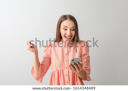 Happy young woman with mobile phone on light background