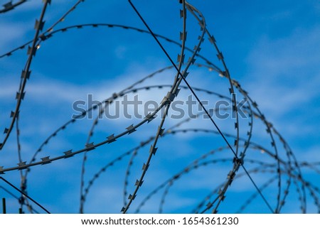 Barbed wire web against the blue sky in light clouds