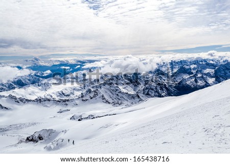 Mountain landscape in autumn or winter in Caucasus Mountains i Russia and Georgia. View from slopes of Mount Elbrus 5642m. Lot of white snow on rocky mountain ridge over blue sunny sky, Russia.
