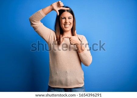 Young beautiful woman wearing casual sweater over blue background smiling making frame with hands and fingers with happy face. Creativity and photography concept.