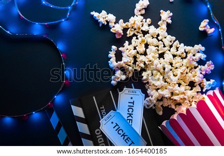 Ticket, popcorn, filmstrip and clapper, movies and entertainment concept on black background with blue neon light, flatlay