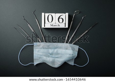 Metal dental tools, wooden calendar with with the date March 6, mask on the face