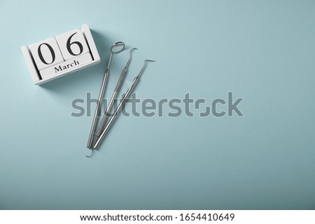 Metal dental tools, wooden calendar with the date March 6, on a blue background