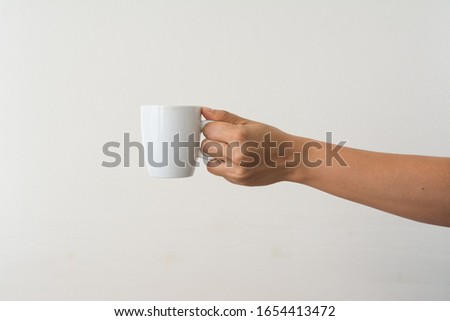Hand holding a white cup on white background Royalty-Free Stock Photo #1654413472