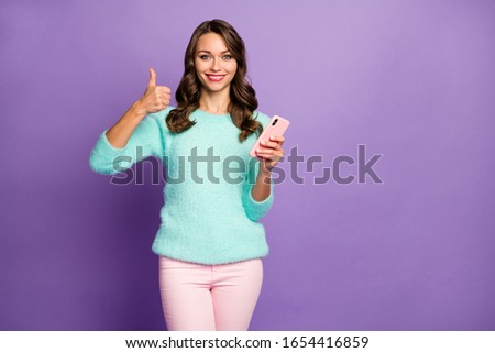 Photo of funny pretty lady hold telephone raise thumb finger up advising smart phone season sale price wear casual fluffy pastel sweater pink pants isolated purple color background