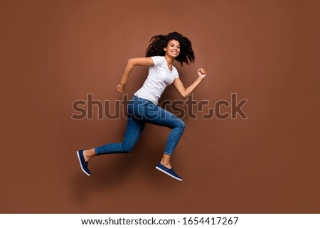 Full length profile photo of funny dark skin lady jumping high sports competitions participant rushing finish line wear white t-shirt jeans isolated brown color background