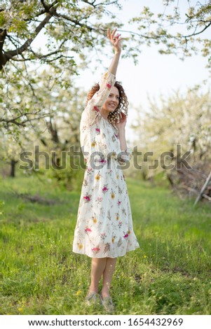 Young attractive girl walks in spring green park enjoying flowering nature.