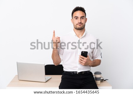 Young business man with a mobile phone in a workplace pointing with the index finger a great idea