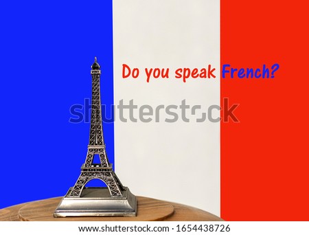 A miniature of the Eiffel Tower on a 
wooden table, written "do you speak French?" Background France flag