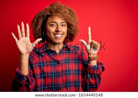 Young beautiful African American afro woman with curly hair wearing casual shirt showing and pointing up with fingers number seven while smiling confident and happy.