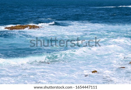 Beautiful waves and white foam on the Aegean sea. Waves crash on the stones. Splash sparkle in the sun. Beautiful blue sea in the background.