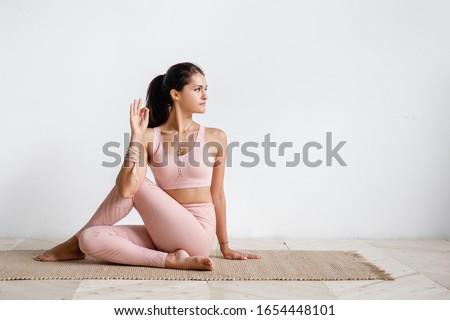 Positive caucasian young brunette woman doing Half lord of the fishes exercise, Ardha Matsyendrasana pose doing yoga. Yoga teacher woman doing gomukhasana on white background. Advertising space Royalty-Free Stock Photo #1654448101