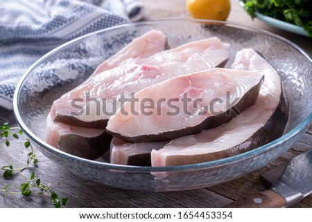 Fresh halibut steaks in a glass bowl on a rustic wood table top.