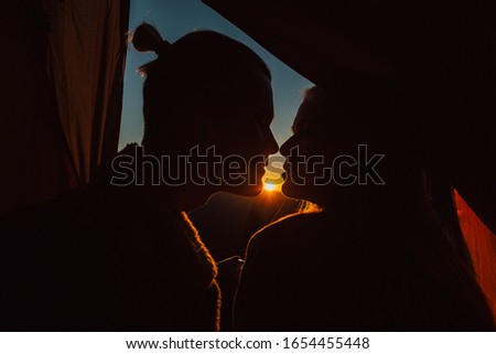 A silhouette of a close up of a woman and man's face. Couple kissing at sunset. Passion.