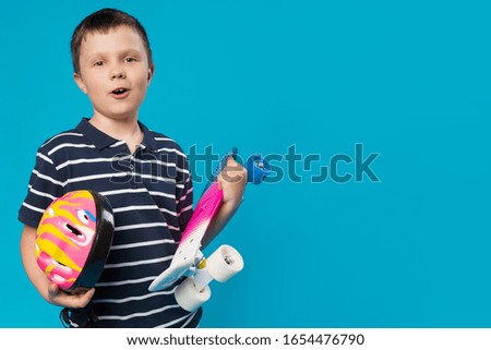 cheerful boy with emotions holding a colored skateboard and safety helmet, concept of active lifestyle, on a turquoise background, copy space