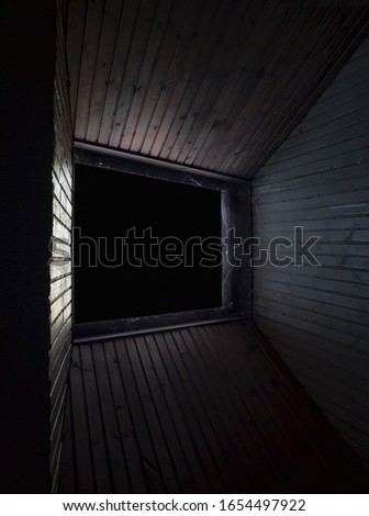 Interesting perspective of window in spooky attic and wooden paneling. Dark and lot of dust.