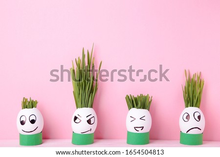 Funny handmade eggs with hair of green grass with copy space. Easter concept on pink backgrund, top view