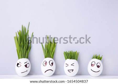 Funny handmade eggs with hair of green grass with copy space. Easter concept on grey backgrund, top view