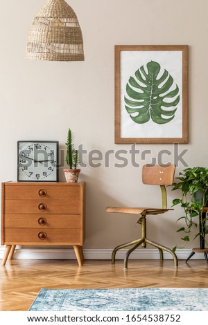 Vintage interior design of living room with stylish retro chair and commode, pendant lamp, plants, cacti, black clock and brown mock up poster frame on the beige wall. Stylish home decor. Template. 