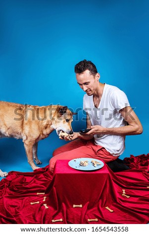 Side view of happy man giving special birthday cake to cute dog against blue background