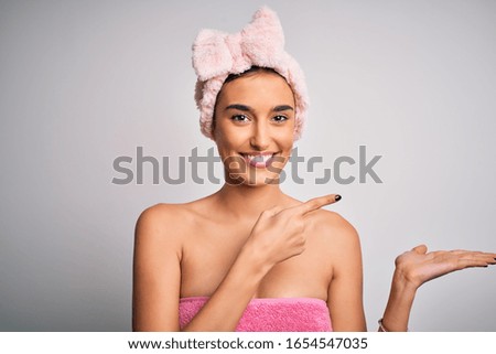 Young beautiful brunette woman wearing towel after shower over isolated white background amazed and smiling to the camera while presenting with hand and pointing with finger.