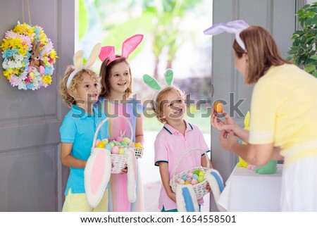 Kids at Easter egg hunt. Child holding basket with colorful chocolate eggs, wearing bunny ears. Little boy and girl at decorated front door after Easter celebration. Children celebrate spring holiday.