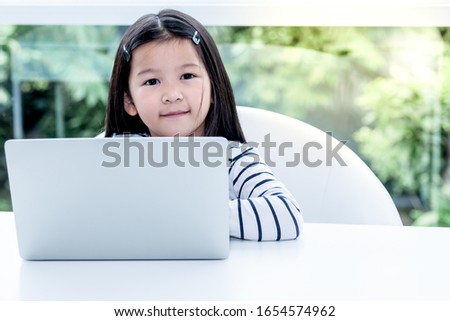 Portrait images of A 6 year old Asian girl are smile and happy while using notebook with determination On White table and blur background, concept to children and communication technology.