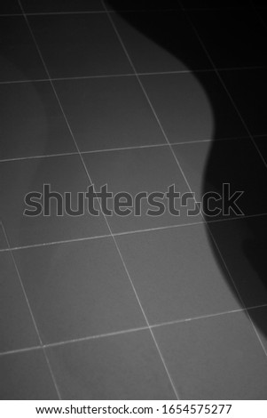 Floor square tile on which a wave-like shadow falls. Background geometric black and white image.