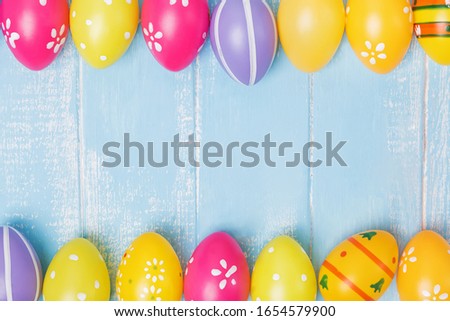 Colorful Easter eggs on blue wooden table with copy space, creative frame