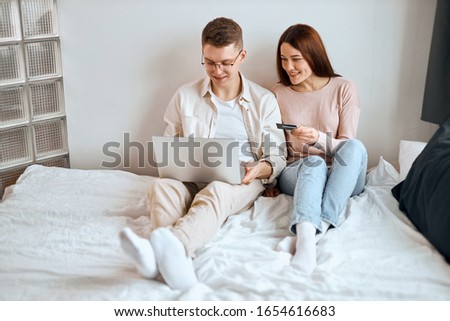 positive couple looking at their accounts online having a rest in the bedroom. close up photo. Finances are good for us.