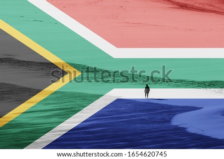 A South African flag with a women walking on a beach in the background. Tourism concept image. 