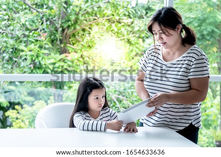 A 6 year old Asian girl is touchy and upset that her mother does not use the tablet For watching cartoons, with blur green tree background, to children and tecthnolygy concept.
