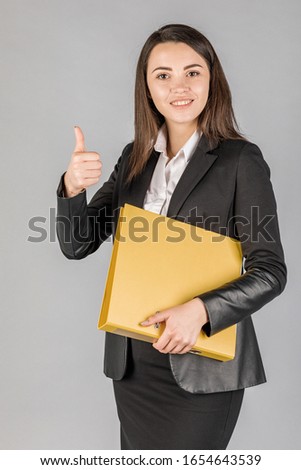Young business woman in dark suite with file on grey background. Office concept