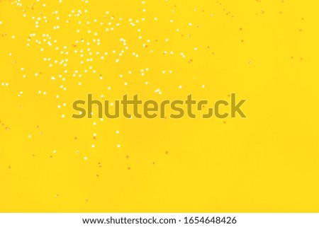 Tiny pearl stars on yellow background. Flat lay, top view.