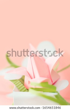 Close up composition of pink origami paper tulip with green decorations in white box with hearts on pink background. Art project. Copy space. DIY concept