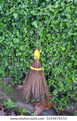 a broom made from several coconut sticks tied with plastic and given a wooden handle.