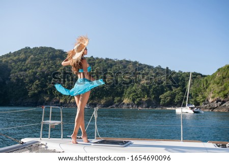 Back view: Beautiful curly brunette woman in a bikini and long blue skirt on the yacht enjoys the  sea view. Luxury travel
