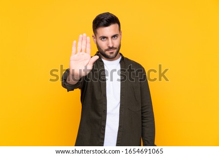 Man over isolated yellow background making stop gesture with her hand