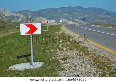 Winding road white and red sign in the mountains. Warning sign and bend in road. Empty road