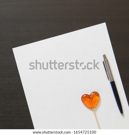Template of white paper with pen and heart shaped caramel on dark wenge color wooden background. Concept of entertaining children's business, leisure for kids. Stock photo with empty space for text.