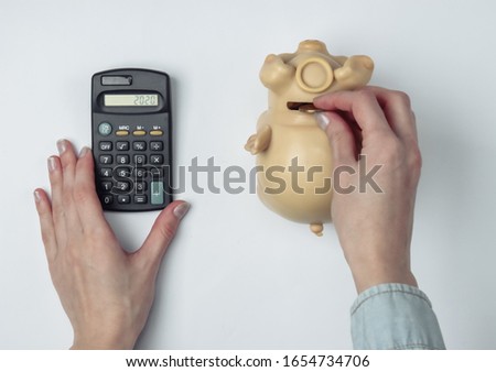 Calculation of the family budget. Female hand uses a calculator and puts a coin in a piggy bank on a gray background. Top view